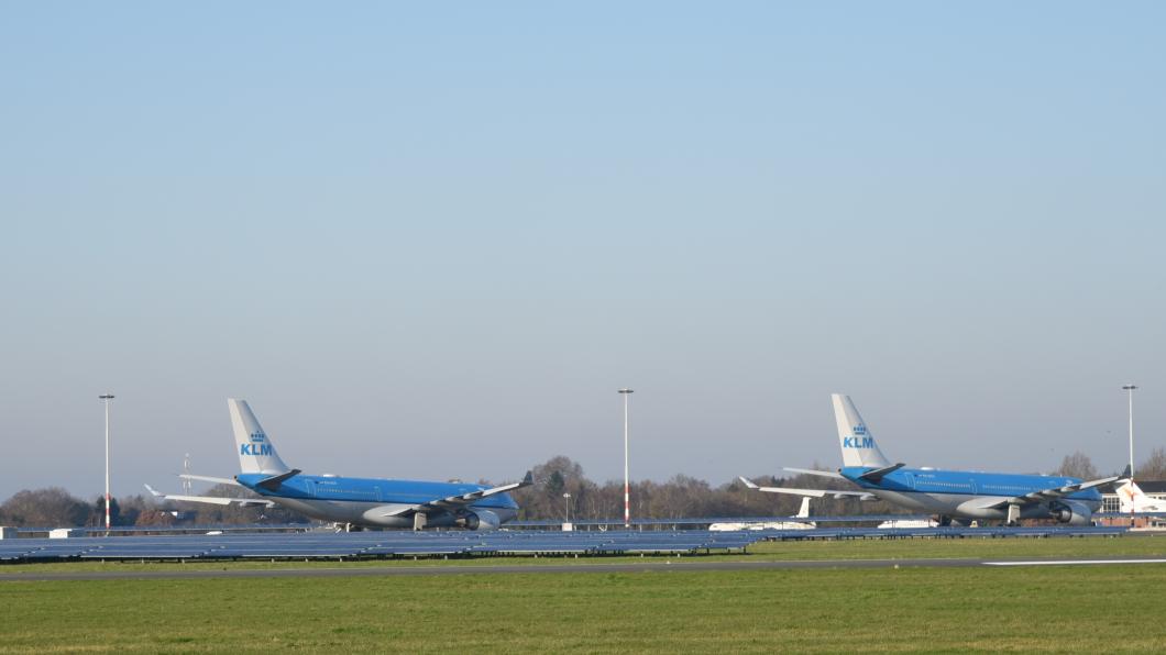 Foto van een landingsbaan op Groningen Airport Eelde, waar twee blauwe KLM vliegtuigen op geparkeerd staan.