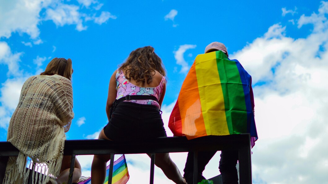 Foto van drie mensen met hun rug naar de camera. De rechterpersoon draagt een Pride-vlag.